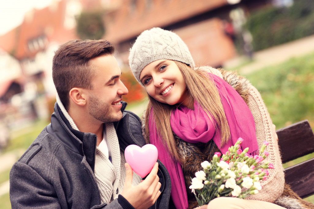Young couple on a date with the boy holding a heart and the girl holding flowers.