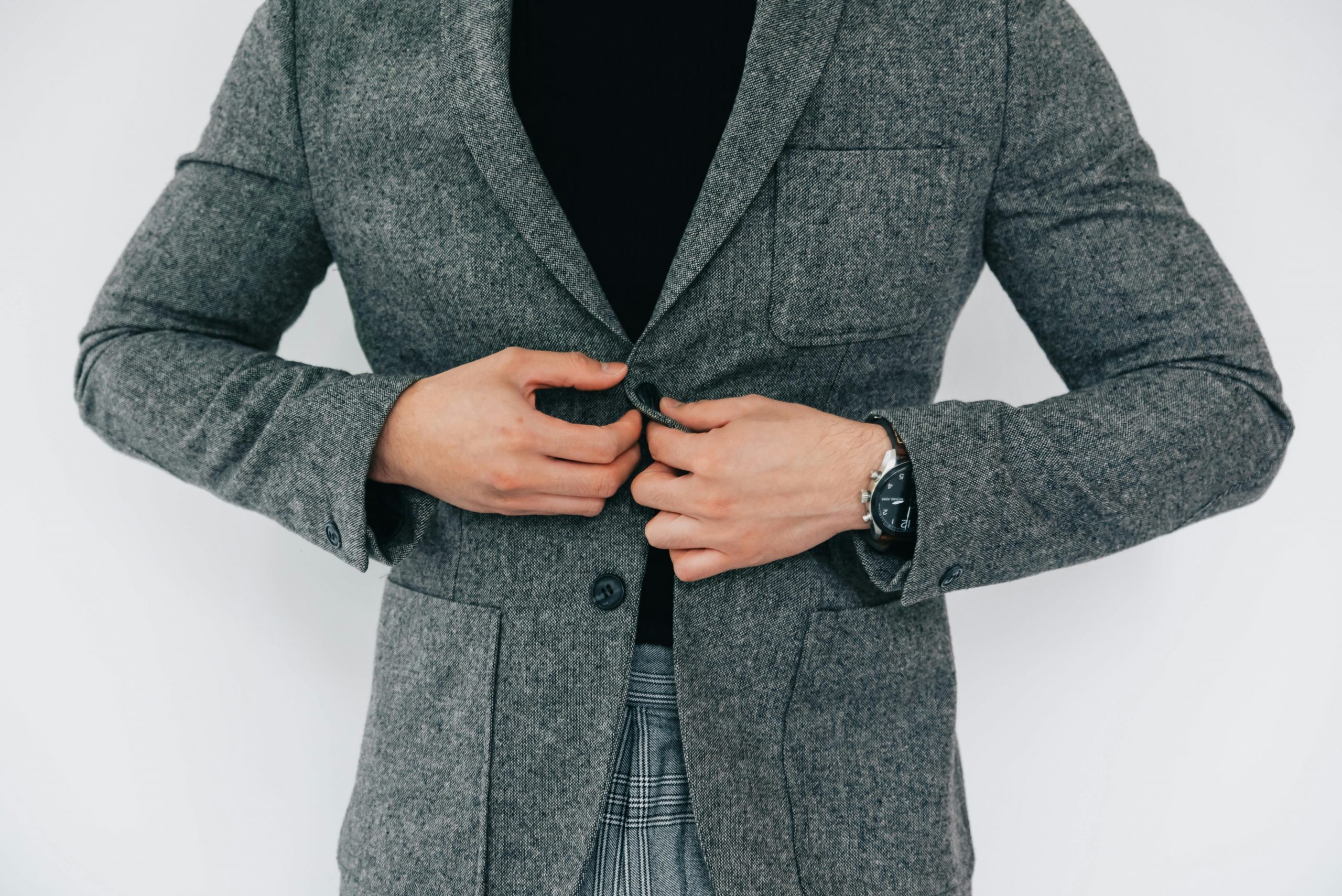 man buttoning a gray blazer over a black top