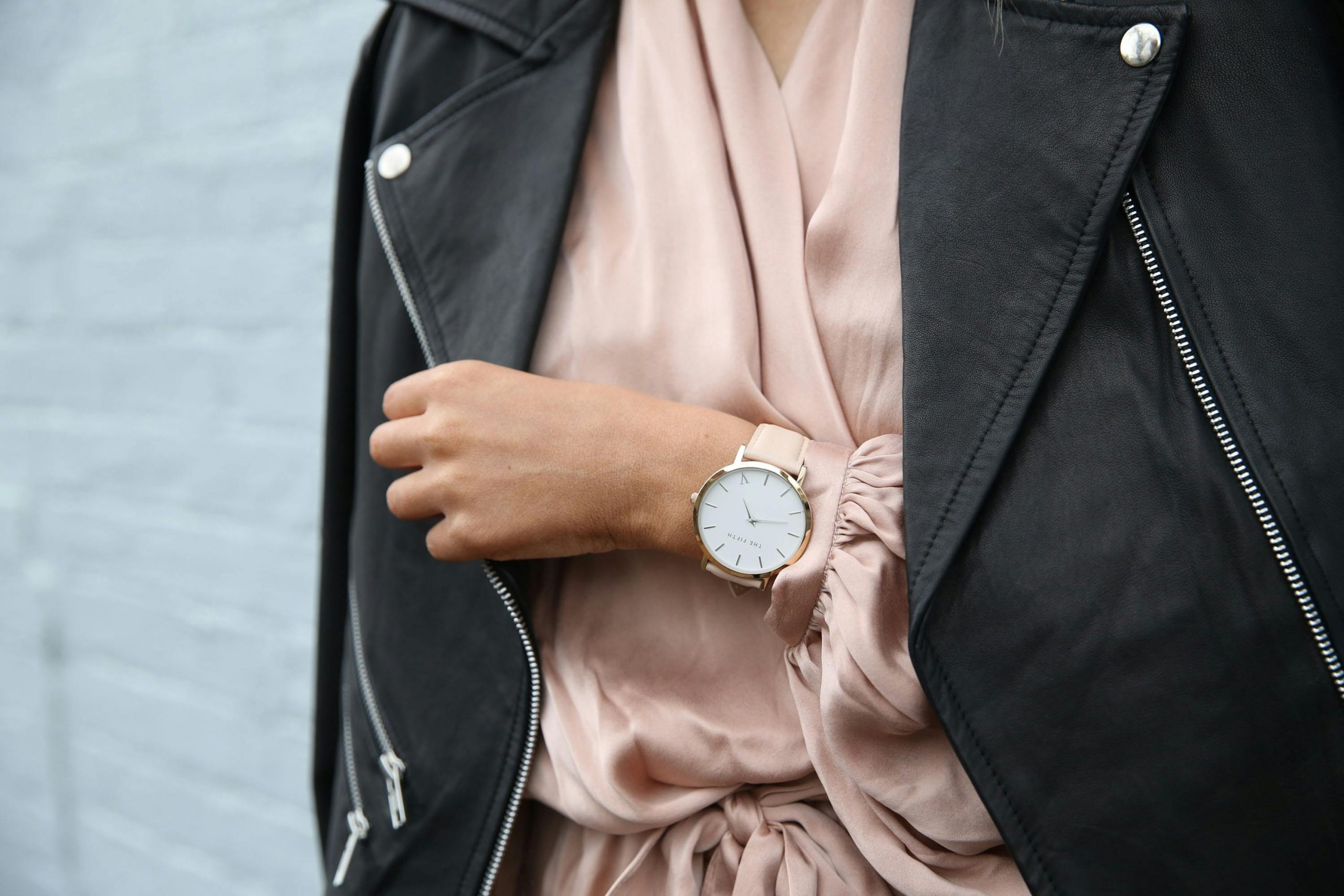 woman wearing a black leather jacket over an old rose silk dress, accessorized with a classy watch